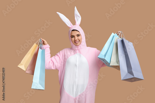 Happy young woman in bunny costume with shopping bags on brown background. Easter celebration