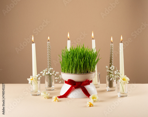 Novruz table setting with green samani wheat grass with red ribbon, daffodils, candles, kelagai and blooming flowers, spring or new year celebration in Azerbaijan, copy space photo