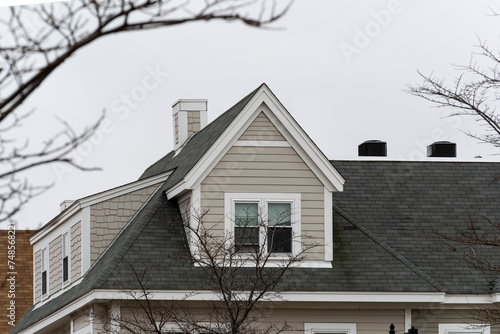 Dormer windows on the sloped shingle roof of a newly built family house on a winter day in Brighton, MA, USA