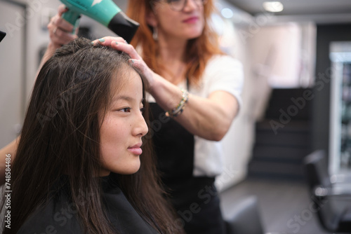 Chinese woman sitting while hairdresser drying her hair