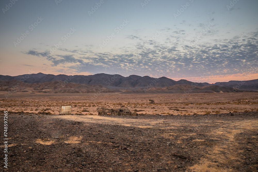 Wooden barn in the desert. Blue hour after sunset behind the mountains in the desert, Egypt Sandy land in the foreground, rocky mountains in the background. Little clouds on the sky during the sunset.