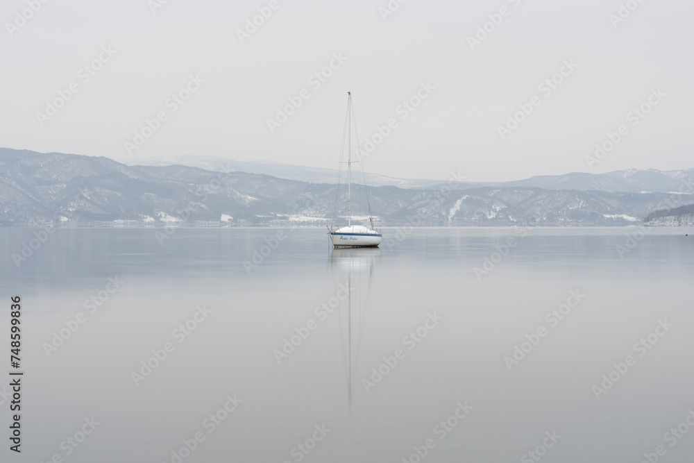 Fototapeta premium lone sailing boat on a like against winter backdrop