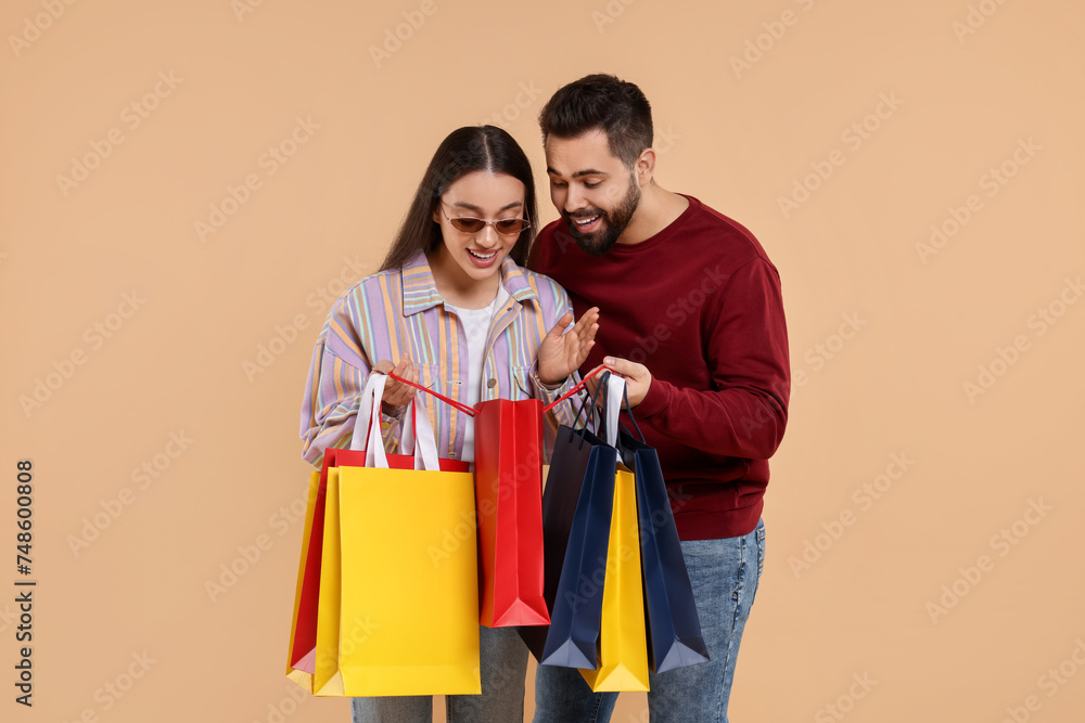 Man showing shopping bag with purchase to his girlfriend on beige background Man showing shopping bag with purchase to his girlfriend on beige background