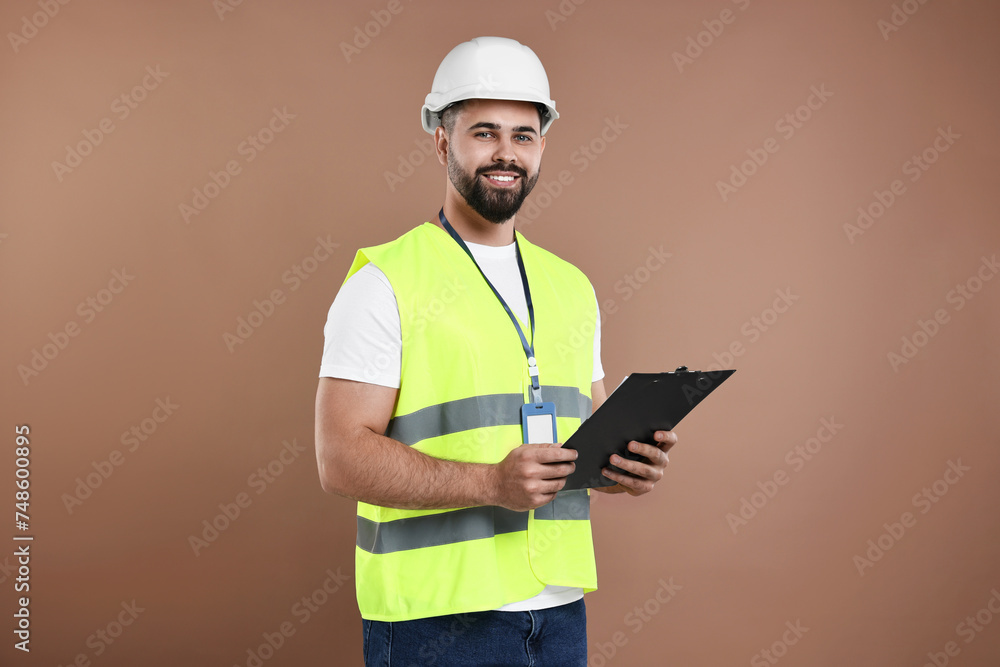 Engineer in hard hat holding clipboard on brown background Engineer in hard hat holding clipboard on brown background