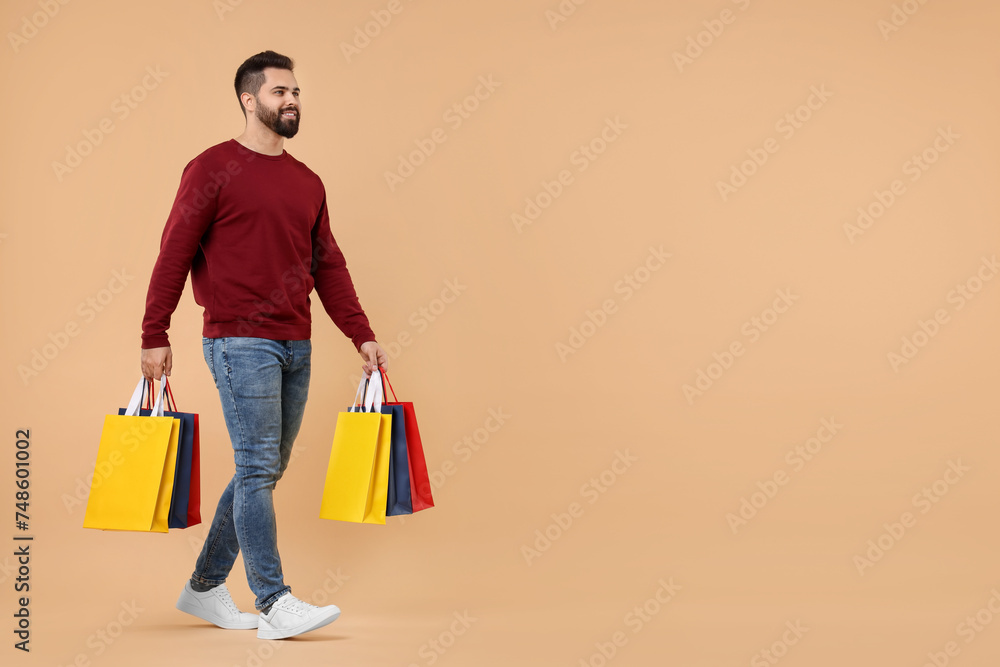 Smiling man with many paper shopping bags on beige background. Space for text Smiling man with many paper shopping bags on beige background. Space for text