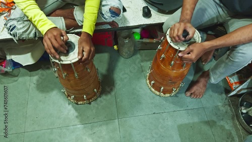 Two people sitting on the floor playing traditional drums with a focus on hands and instruments man repairing drum at musical workshop photo