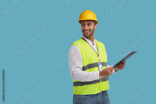 Engineer in hard hat holding clipboard on light blue background  space for text