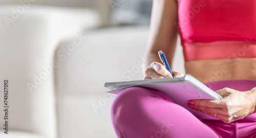 Sporty woman sits on a mat and writes down future training plans for achieving sports results
