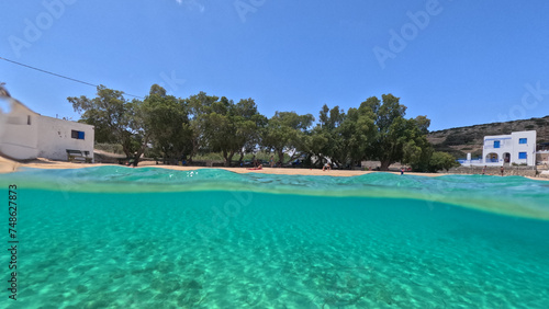 Underwater split photo of paradise crystal clear sea beach of Agios Georgios in main port of Irakleia island covered in Armirikia trees providing natural shade, small Cyclades, Greece © aerial-drone