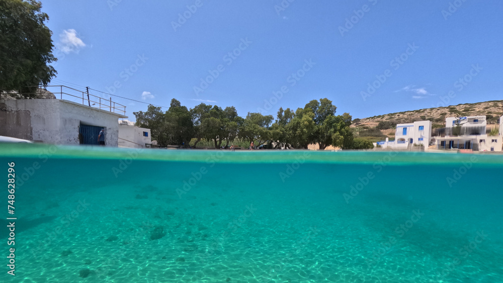 Obraz premium Underwater split photo of paradise crystal clear sea beach of Agios Georgios in main port of Irakleia island covered in Armirikia trees providing natural shade, small Cyclades, Greece