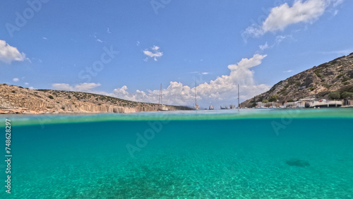 Underwater split photo of paradise crystal clear sea beach of Agios Georgios in main port of Irakleia island covered in Armirikia trees providing natural shade  small Cyclades  Greece