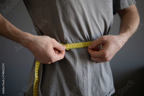 Man Measures Waist Circumference With Yellow Tape During Fitness Check