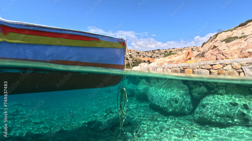 Underwater split photo of traditional wooden fishing boat anchored in turquoise sea of rocky bay in island of Crete, Greece