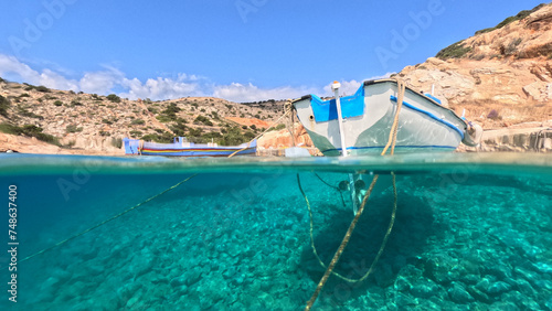 Underwater split photo of traditional fishing boat anchored in small secluded fjord and paradise beach of Tourkopigado, Iraklia island, Small Cyclades, Greece