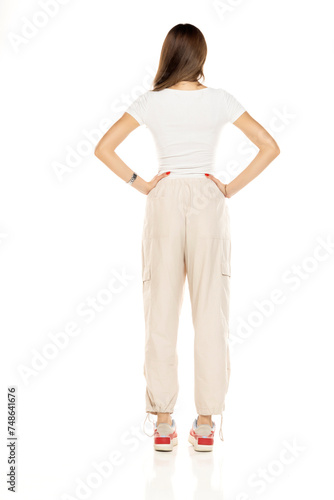 Cute brunette woman in white shirt and loose white trousers posing on a white background. Full length, back, rear view.