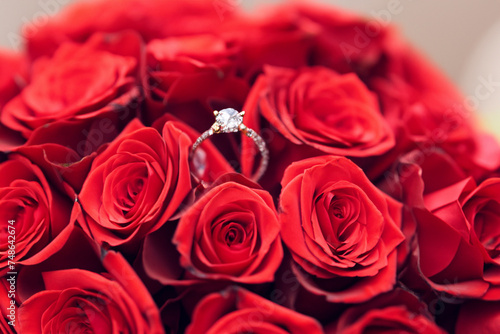 ring proposal. a small silver ring with a stone lies on a beautiful red bouquet of roses  close-up  creative concept