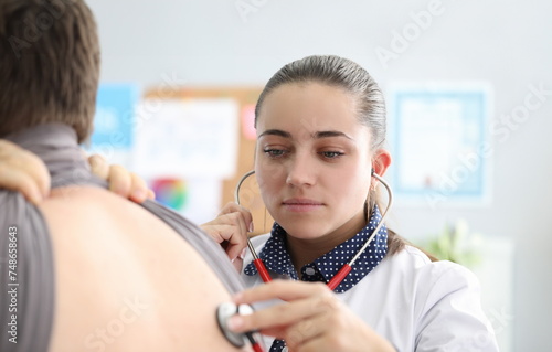 Woman therapist in clinic listens to lungs man. Patient is referred to general practitioner or general practitioner. Primary examination and listening to lungs. Palpation specific areas certain organs