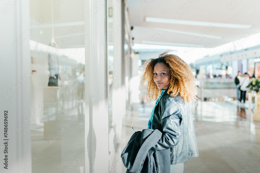 A young black girl walking between stores in a shopping center window shopping. Look at camera. White background with slight overexposure