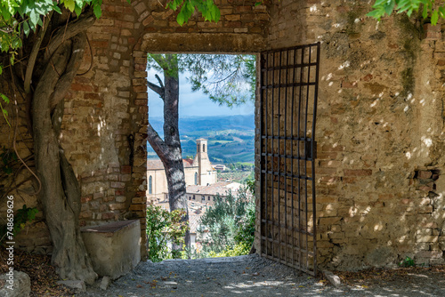 View through the opening of a door in the fortified wall in Parco della Rocca of San Gimignano, Italy with view on Chiesa di Sant Agostino and typical Tuscan landscape photo