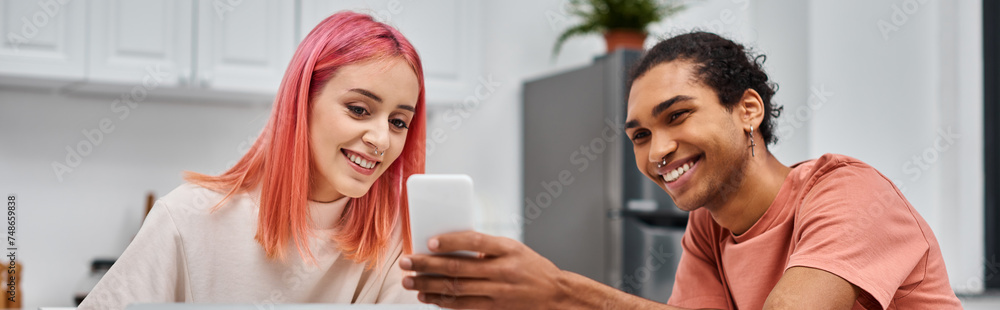 loving multiracial couple in casual attires working at home and looking at smartphone, banner