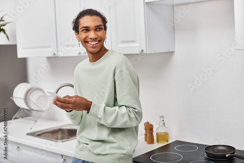 handsome joyful african american man in white casual sweater holding smartphone and looking away