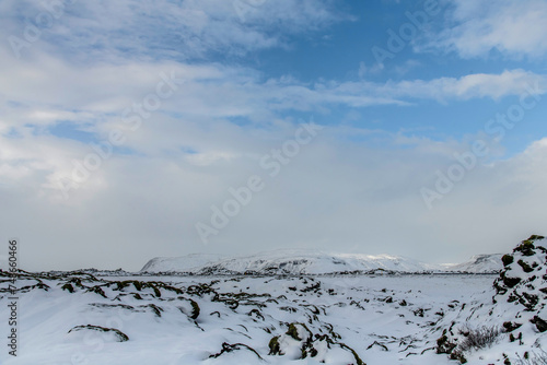 Panoramic low angle winter landscape in Iceland with white clouds over snowy and icy hilly landscape with bright sun on white snow landscape of lava rock