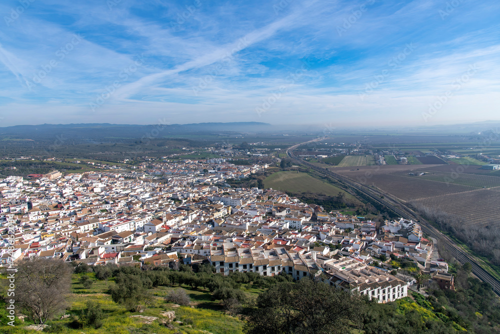Panoramic high level view over the city of Almodovar del Rio, Cordoba, Andalusia, Spain with characteristic white houses and view over the agricultural landscape against a white clouded blue sky