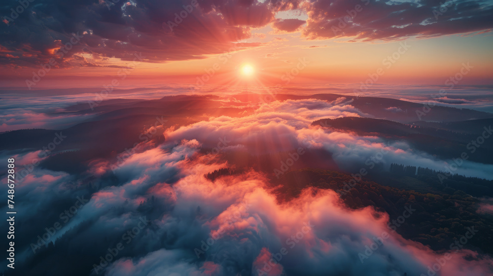 A breathtaking aerial view of a misty mountain landscape bathed in the warm glow of a rising sun. The sunlight pierces through the clouds, casting rays and illuminating the undulating hills below.
