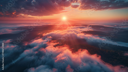 A breathtaking aerial view of a misty mountain landscape bathed in the warm glow of a rising sun. The sunlight pierces through the clouds, casting rays and illuminating the undulating hills below.