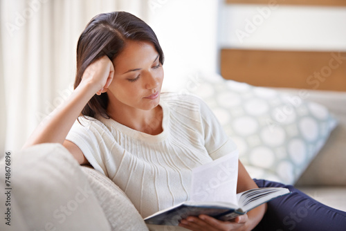 Woman, sofa and reading with book in relax for story, literature or leisure in living room at home. Female person sitting on couch with novel for knowledge, education or learning in lounge at house photo
