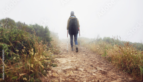 Person, hiking and back in field with trekking sticks, adventure and support for fog trail in mountain. Athlete, backpack and sport gear for safety in wet environment, healthy and walking for fitness © Mariusz/peopleimages.com
