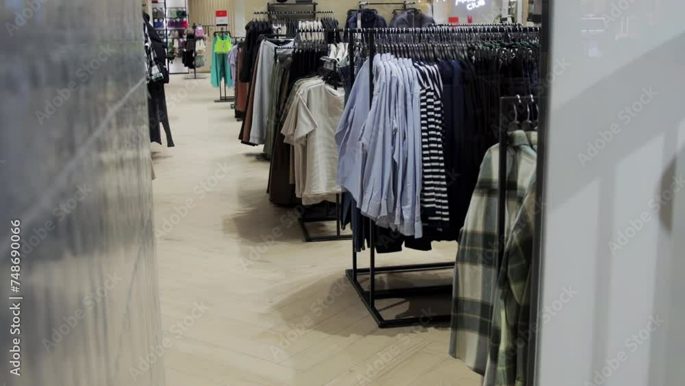 A lot of clothes, T-shirts and shirts hanging on hangers are sold in a modern clothing store, stylish interior. Slow motion A lot of clothes, T-shirts and shirts hanging on hangers are sold in a modern clothing store, stylish interior. Slow motion