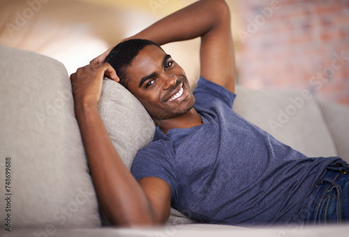 Man, portrait and happiness on sofa with relax in living room of home with comfort, confidence or weekend. Student, african person and smile with face on couch in lounge for rest, day off or wellness