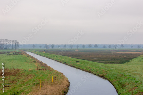 Winter countryside landscape, Typical Dutch polder with green meadow under cloudy sky and cold day, Flat and low land with small canal or ditch and the grass field, North Brabant province, Netherlands