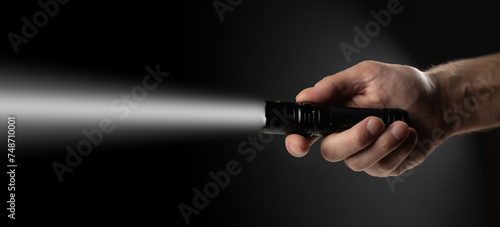 Black flashlight in human hands on a black background, including a white beam