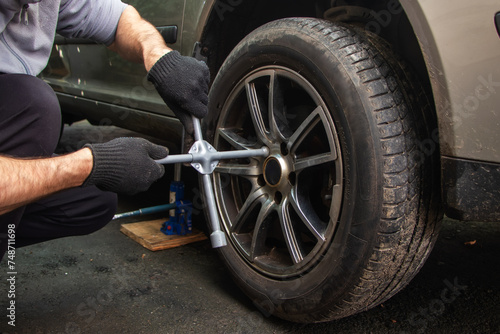 Car mechanic hand using cross wrench to uninstallation the wheel nuts for changing alloy wheel of car.
