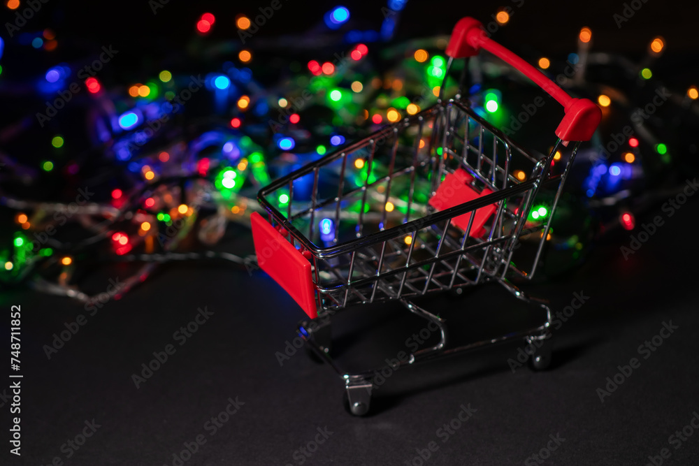 New year shopping. Shopping cart on Christmas garland light background.