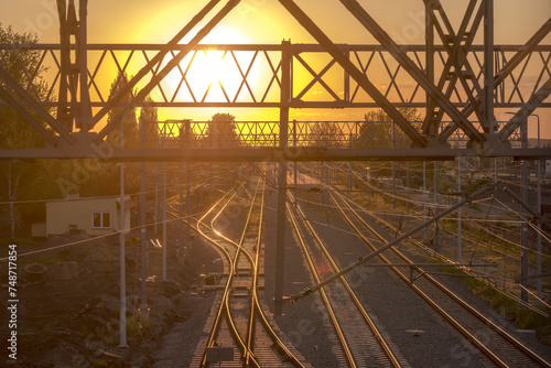 Kolorowy zachód słońca nad torami kolejowymi w Ostrowcu. Konstrukcje metalowe i tory kolejowe zanurzone w złotych promieniach zachodzącego słońca w majowy wieczór.
