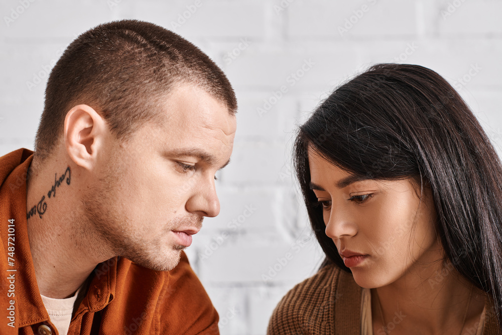 Naklejka premium young and upset interracial couple talking in living room at home at home, relationship difficulties