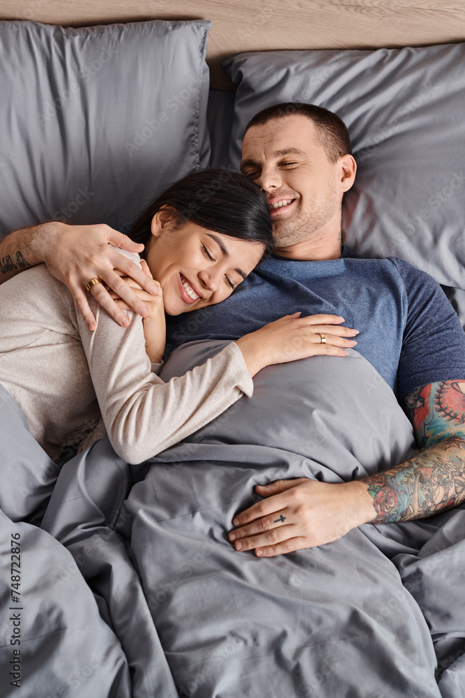 top view of young joyful multicultural couple embracing in bedroom at home, family happiness top view of young joyful multicultural couple embracing in bedroom at home, family happiness