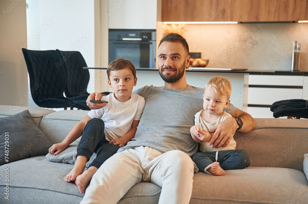 Conception of relaxation. Father with two baby boys is sitting at sofa Conception of relaxation. Father with two baby boys is sitting at sofa