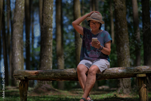 A woman sitting on a wooden bench is video calling while one of her hands is on her hat; smiling, happy face photo