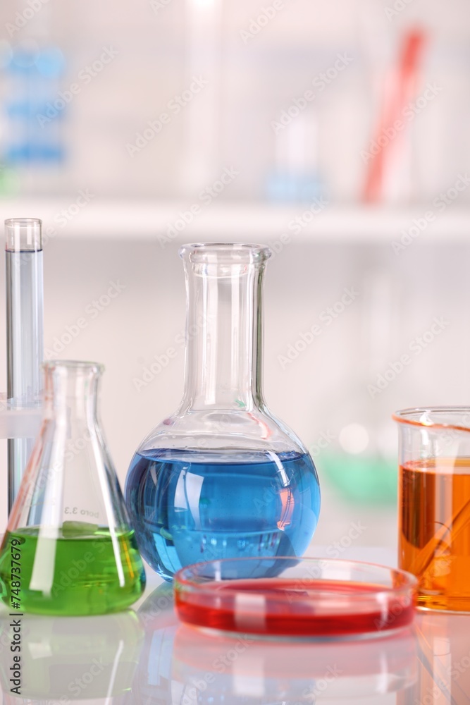 Laboratory analysis. Glass flasks and Petri dish with liquids on white table against blurred background Laboratory analysis. Glass flasks and Petri dish with liquids on white table against blurred background