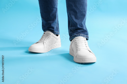 Man wearing stylish white sneakers on light blue background, closeup © New Africa