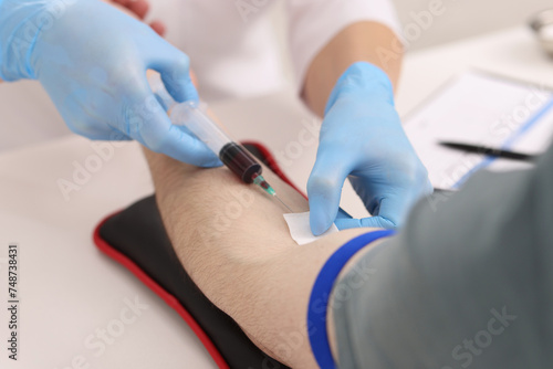 Doctor taking blood sample from patient with syringe at white table in hospital, closeup