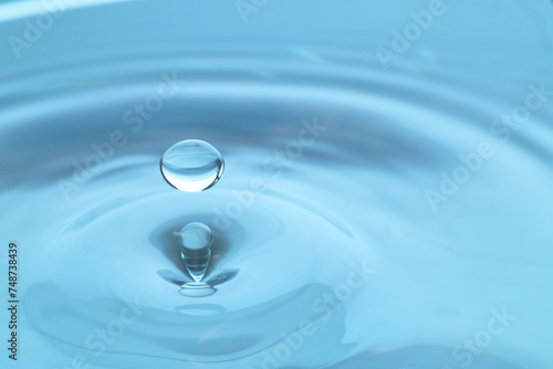 Drop falling into clear water on light blue background, closeup