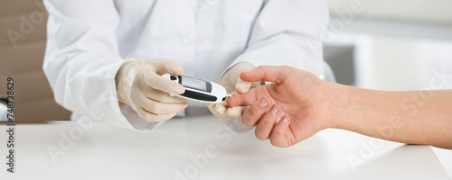 Endocrinologist checking patient's blood sugar level with digital glucometer at table, closeup. Banner design