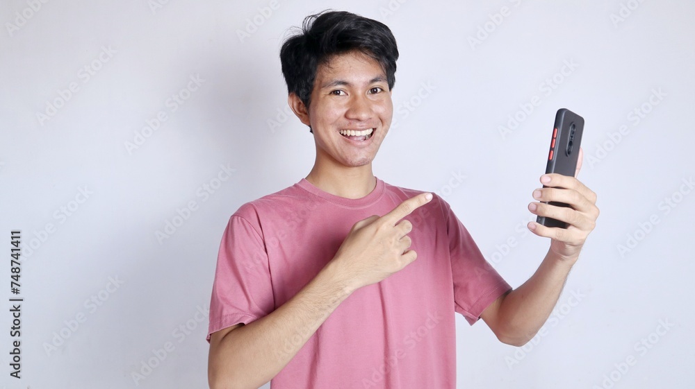 excited asian man with gesture holding and pointing at smartphone excited asian man with gesture holding and pointing at smartphone