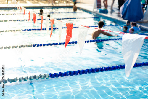 Backstroke flags and blurred swimming class for little kids with coach and parents audience at public competitive swimming pool summertime in Dallas, Texas, pool lane divider rope and floats