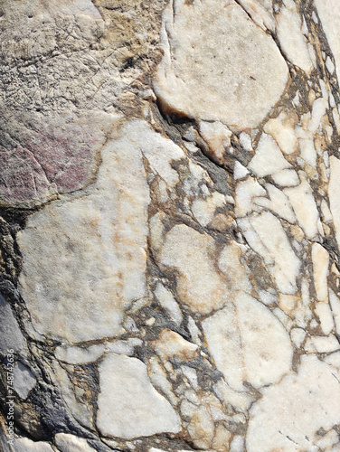 The texture of an old stone wall with pieces of white marble and gray pebbles, with cracks and veins